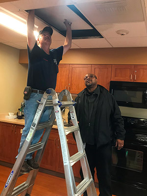 A facilities employee fixes a ceiling tile